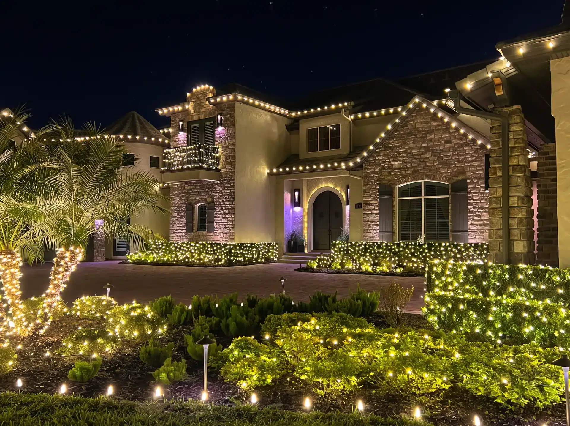 Stone house with roofline Christmas lights and illuminated hedges and landscaping