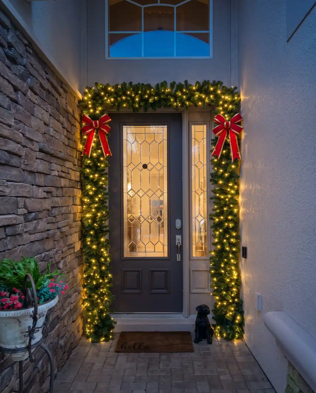 Front door decorated with a lighted Christmas garland and red bows