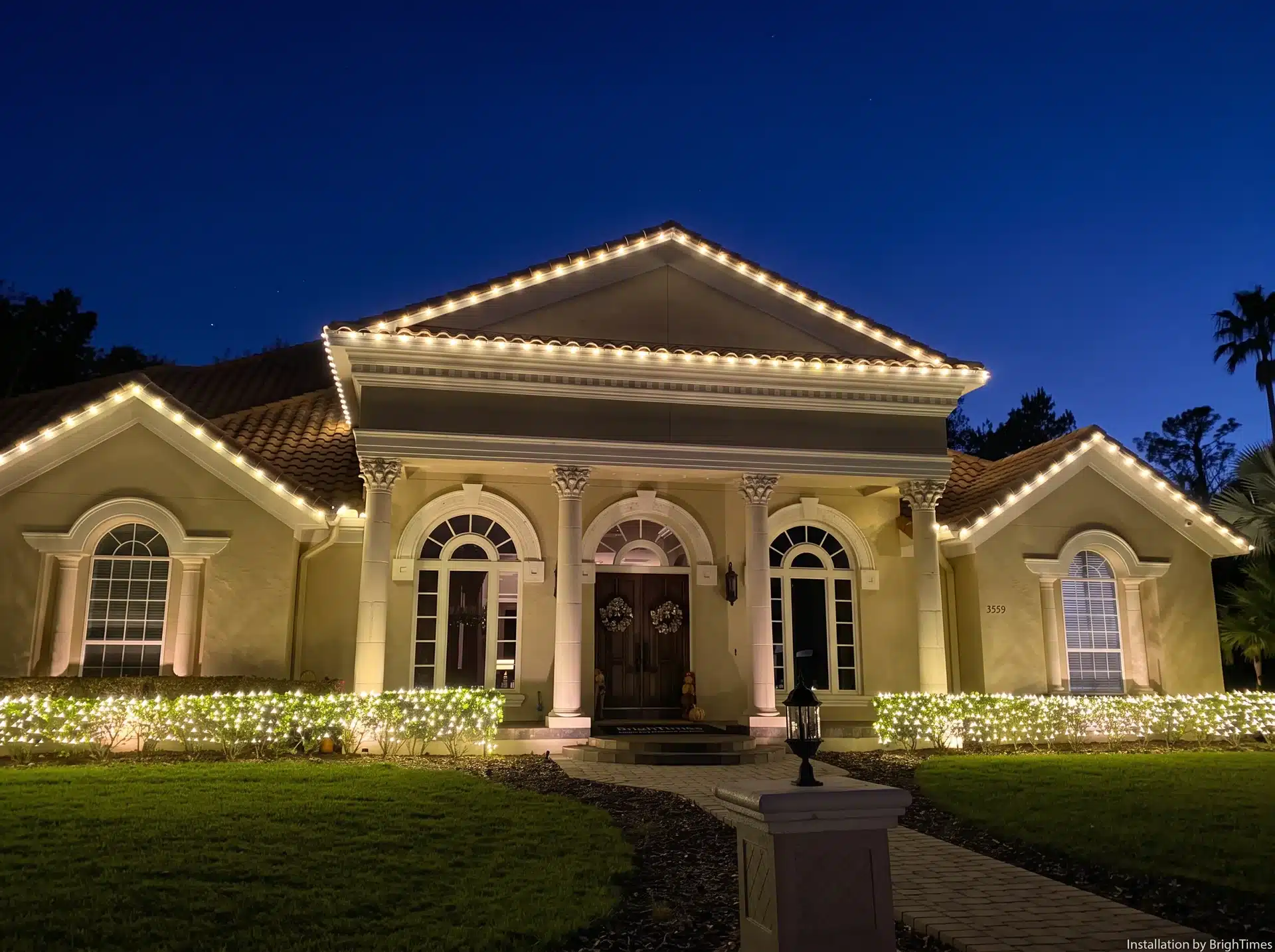 Classic single-story home with warm white roofline Christmas lights and lighted hedges